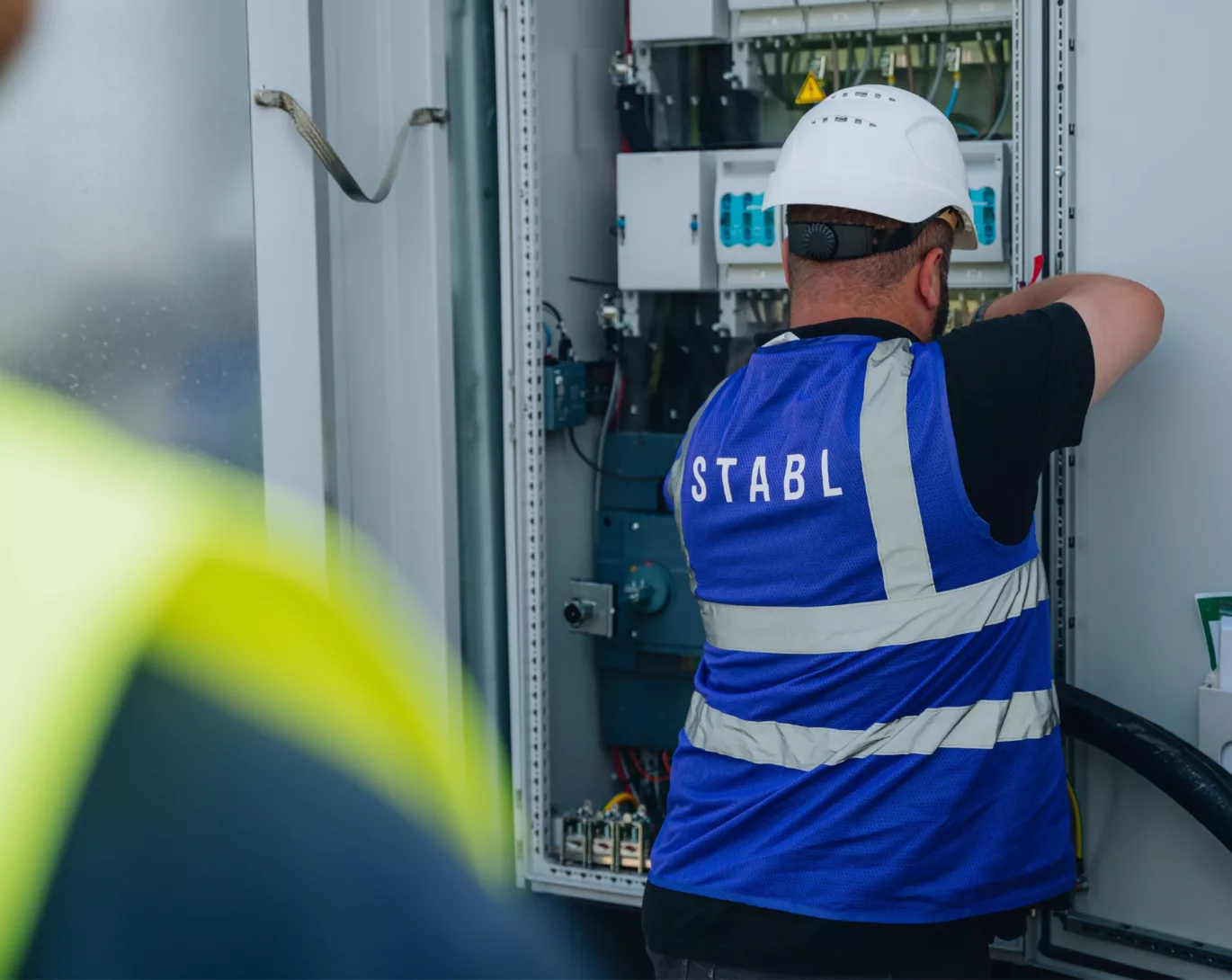 Mitarbeiter von STABL Energy bei Installationsarbeiten mit einem Blick ins Innere des Schaltschranks des Batteriespeichers
